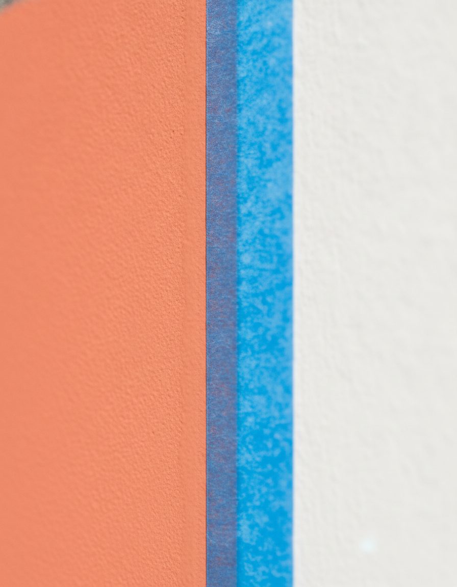 A razor-crisp masked paint line where warm coral meets clean white on a smooth exterior wall